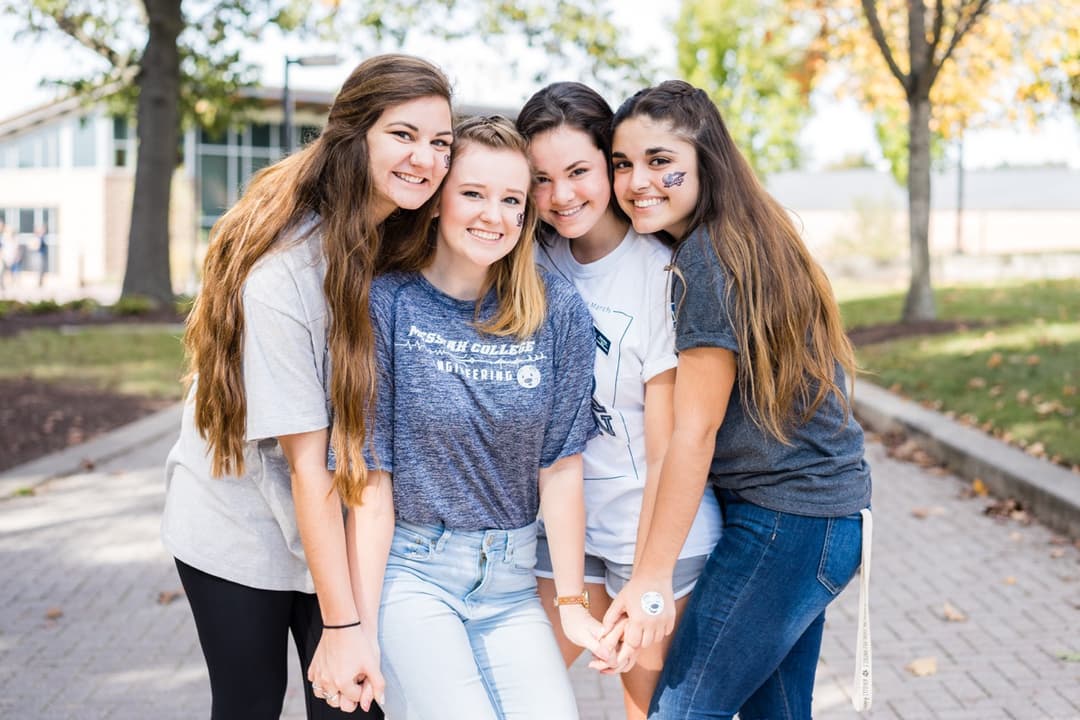 Group of friends smiling together on brick pathway during campus event