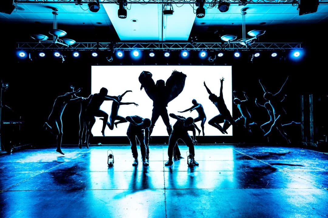 Dance performance silhouettes against blue-lit backdrop with projected animations