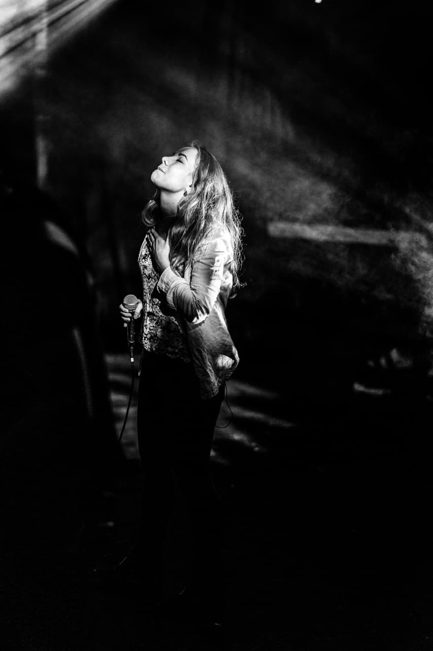 Black and white concert photography: Female singer performing with microphone under stage lights at live show
