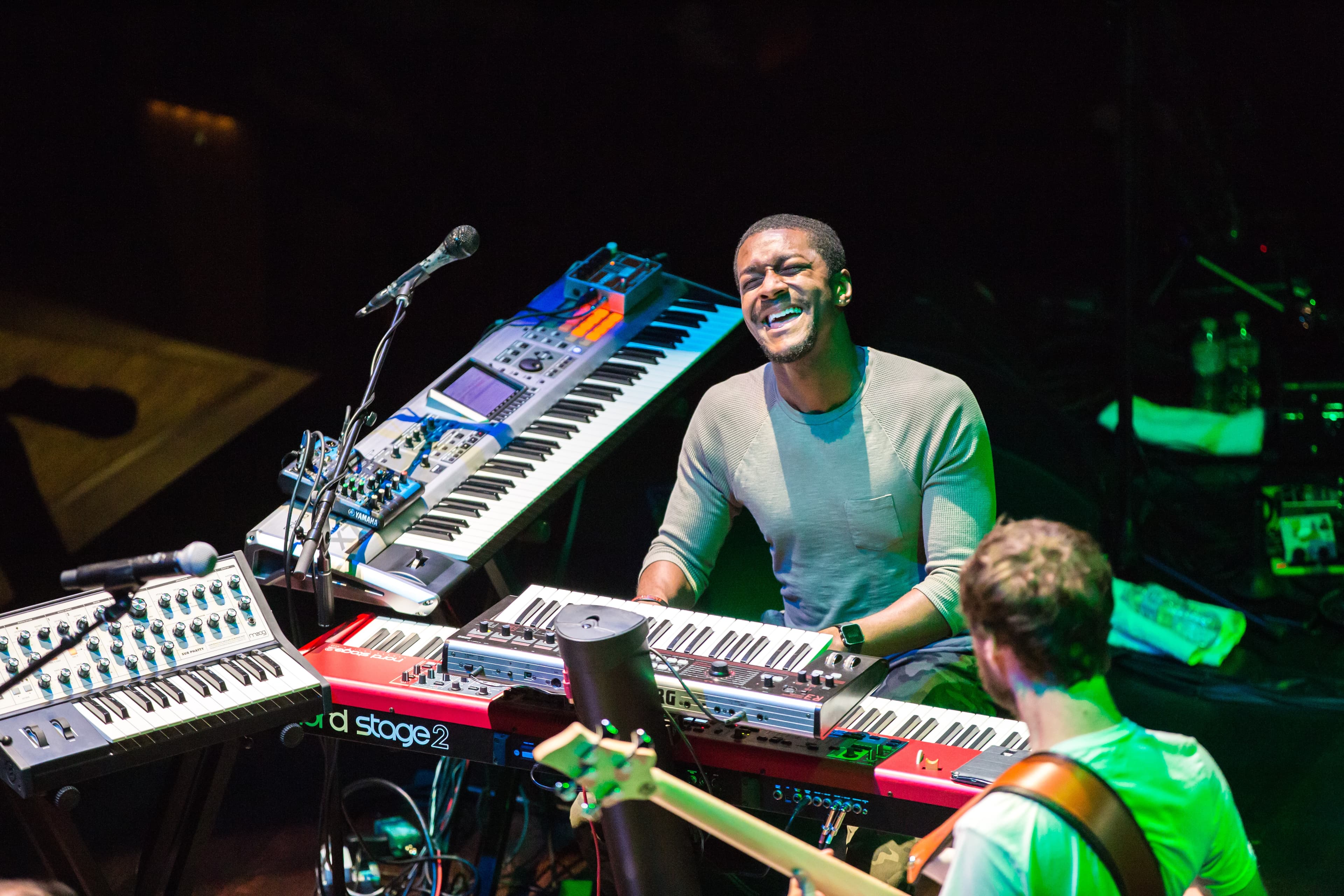 Musician performing live with multiple keyboards and synthesizers under stage lighting