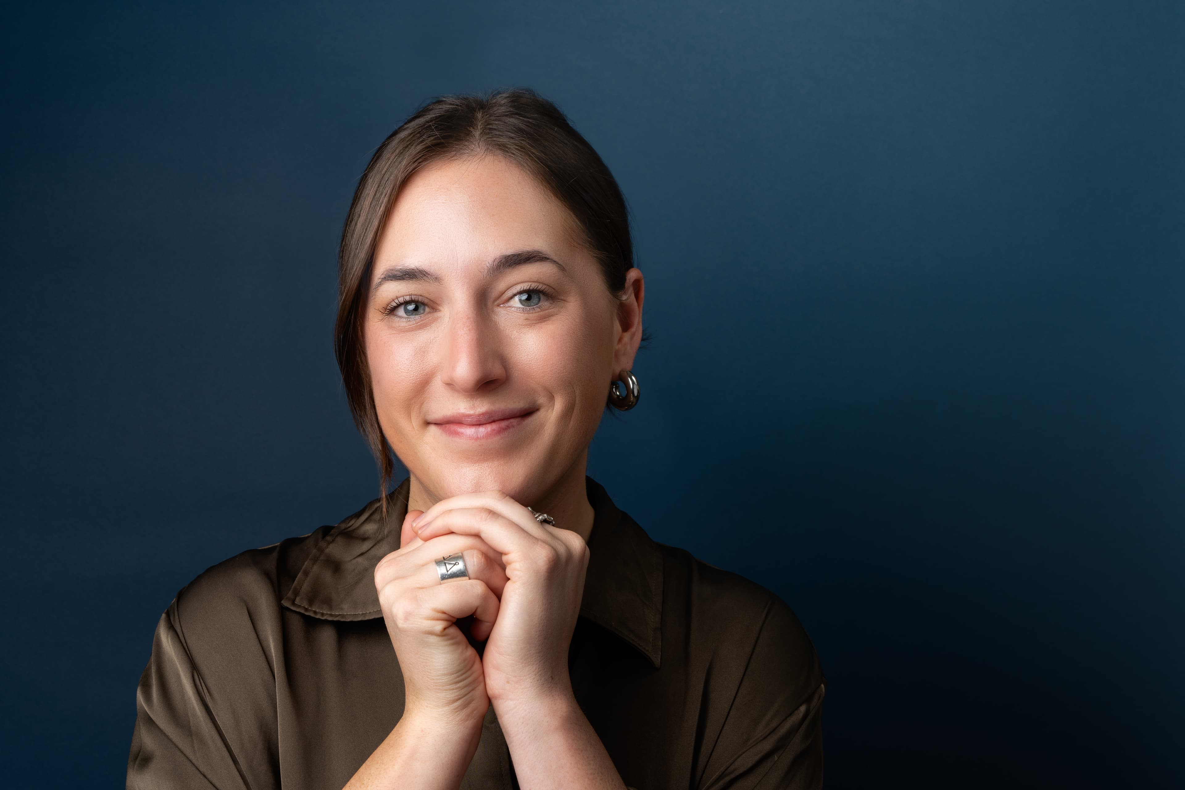 Professional headshot of a person in a brown jacket against a dark blue background